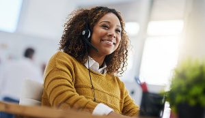 Smiling cloud phone support worker sitting at her desk with her phone headphones on