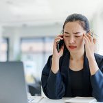Woman in blue suit on her phone rubbing the side of her head like she has a headache