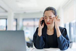 Woman in blue suit on her phone rubbing the side of her head like she has a headache