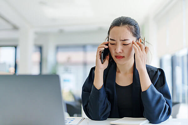 Woman in blue suit on her phone rubbing the side of her head like she has a headache