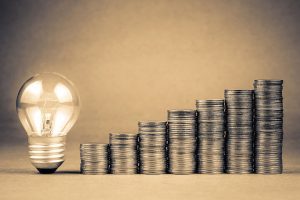 Light bulb next to stacks of coins, each stack higher than the one next to it, to represent savings with IP phones for small business