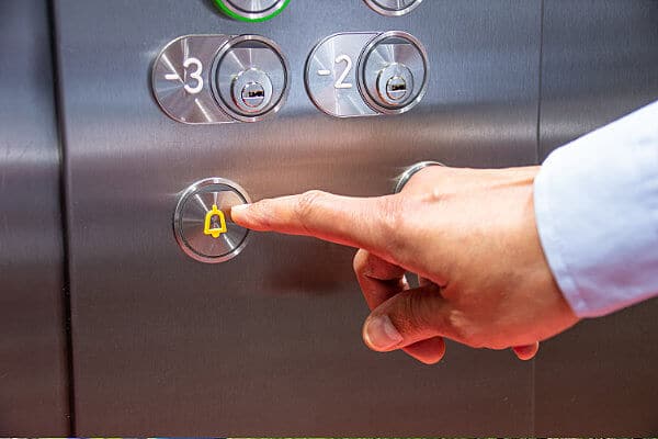 Man pressing the elevator phone or call button. AirDial by FluentStream, a POTS line replacement solution for businesses, can help keep this critical alarm system connected.