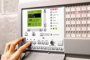 Person pressing a button on a business alarm system control panel. AirDial provides an all-in-one POTS line replacement for old emergency systems during the copper transition.