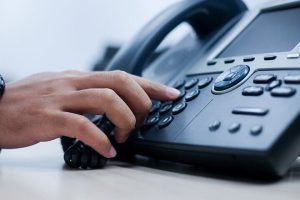 Close up of someone reaching for a business phone, Cloud PBX for SMB
