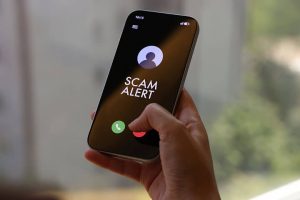 Closeup of person holding a phone with a caller ID showing Scam Likely on the screen