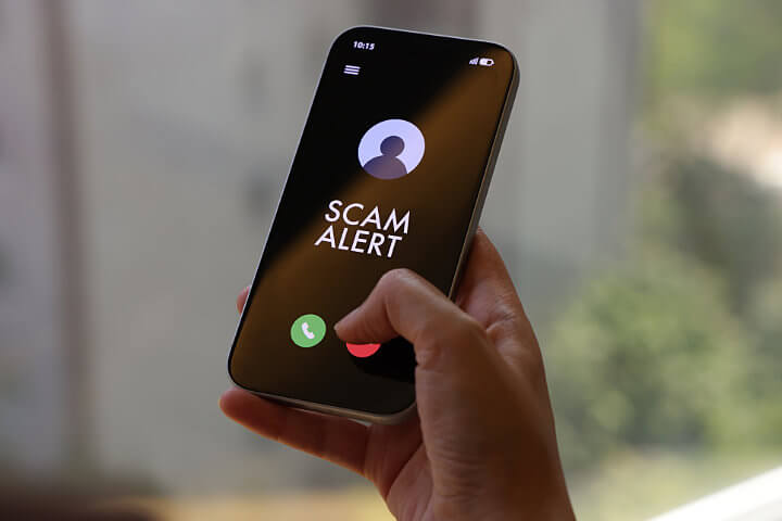 Closeup of person holding a phone with a caller ID showing Scam Likely on the screen