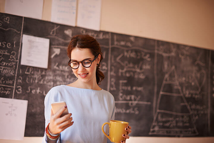 School teacher in front of a blackboard looking at her mobile phone that uses VoIP for schools