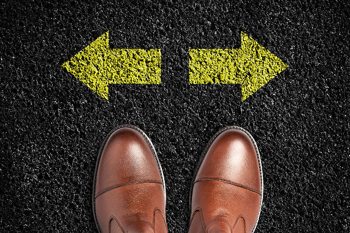 Looking down at to tops of a man's shoes in front of two yellow arrows pointing left and right representing VoIP phone service for small business descisions