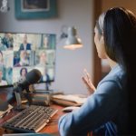 Woman at a desk using webinar best practices while giving a video presentation in front of many people