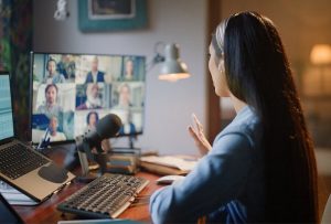 Woman at a desk using webinar best practices while giving a video presentation in front of many people