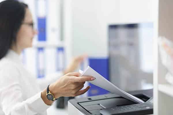 Woman feeding paper into a fax machine. AirDial by FluentStream, a POTS line replacement solution for businesses that helps keep this business fax machine running securely.